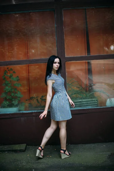 Junge schlanke, charmante Dame posiert in einem kurzen schwarzen und weißen Kleid mit Streifen. schöne und sexy Brünette demonstriert Mode-Pose auf dem Hintergrund der verlassenen Gebäude lizenzfreie Stockbilder