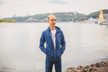 Çekici bir genç adam rahat bakmak nehir kenarında yürüyüş ile kentsel ve modern arka plan