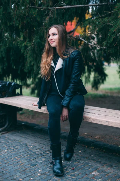 Porträt einer schönen blonden jungen kaukasischen Frau in einer schwarzen Pelzjacke kalten Herbstfrühling. Nahaufnahme, Vintage cremegelb, sitzt auf der Bank im Herbstpark — Stockfoto