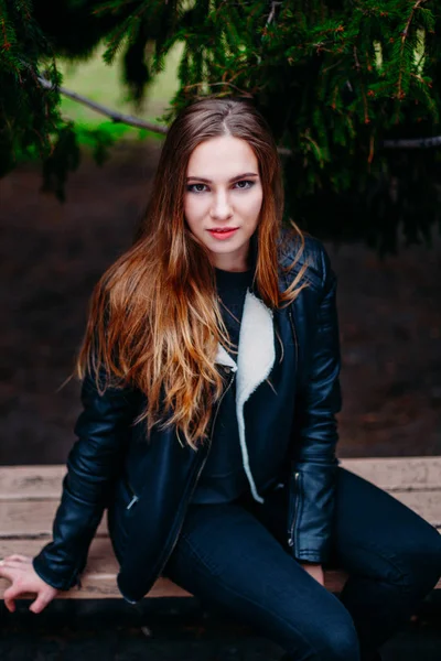 Potret seorang wanita muda berambut pirang yang cantik dengan jaket bulu hitam musim semi yang dingin. closeup, vintage warna kuning krem, duduk di bangku di taman musim gugur — Stok Foto