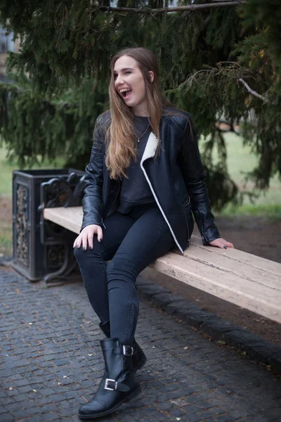 Porträt einer schönen blonden jungen kaukasischen Frau in einer schwarzen Pelzjacke kalten Herbstfrühling. Nahaufnahme, Vintage cremegelb, sitzt auf der Bank im Herbstpark — Stockfoto