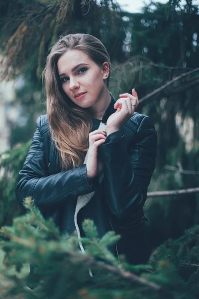 Porträt einer schönen blonden jungen kaukasischen Hipsterin in einer schwarzen Pelzjacke, die modisch in Tannenzweigen posiert. lächelnde glückliche Frau, kalter Herbst oder Frühling — Stockfoto