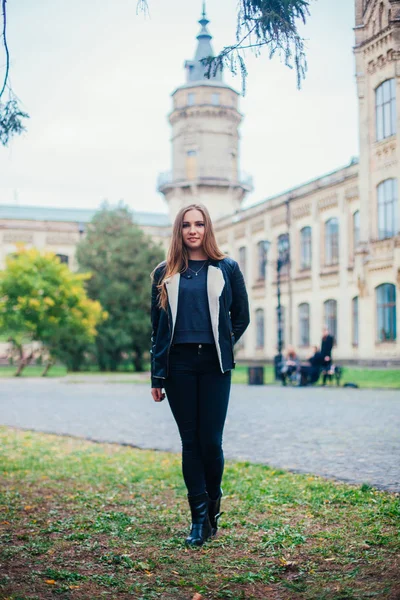 Módní portrét krásné blond mladé kavkazské ženy v černém kožešiny bunda studené podzimní pobyty jaro. pózuje vedle věže — Stock fotografie