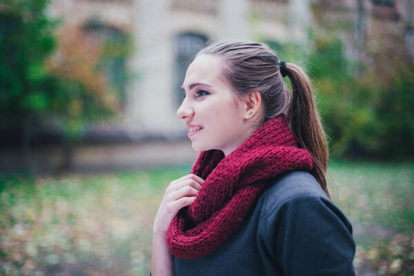 Portrait fashion of a beautiful blonde young caucasian woman cold Autumn getaways spring. autumn park, red green yellow threes. In a burgundy cap and scarf. Embarrassed,  Dreamy beautiful girl