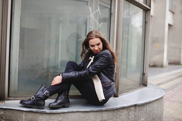 Ritratto di una bella bionda giovane donna caucasica hipster In una giacca di pelliccia nera in posa di moda accanto all'edificio di vetro blu. ritratto urbano della città — Foto Stock