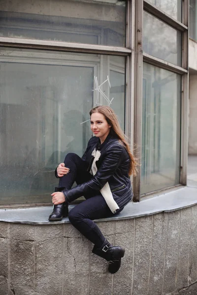 Ritratto di una bella bionda giovane donna caucasica hipster In una giacca di pelliccia nera in posa di moda accanto all'edificio di vetro blu. ritratto urbano della città — Foto Stock