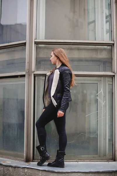 Porträt einer schönen blonden jungen kaukasischen Hipsterin in einer schwarzen Pelzjacke, die neben dem blauen Glasgebäude posiert. Stadtporträt urban — Stockfoto