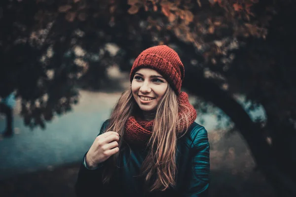 Portrait-Mode einer schönen blonden jungen kaukasischen Frau kalten Herbst Kurzurlaube Frühling. Herbstpark, rot grün gelb dreier. in weinroter Mütze und Schal. peinlich, verträumt schönes Mädchen Stockbild