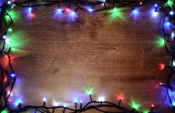 New-year electric garland on a wooden background. Bright bulbs on a wooden table and Christmas tree. — Stock Photo, Image