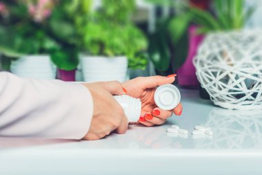 Pills, medicine, drugs on the table. Woman is holding her hands on the table and around the scattered white drugs. Reaches for drugs, is sick, taking large amounts of medication. Medicine concept. clipart