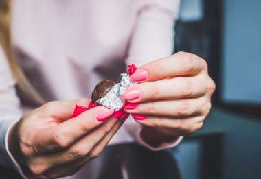 Chocolate in woman's hands, opening chocolates. A woman holds in her hand a chocolat, a blank, worn out chocolatier, eating chocolate, obesity, unhealthy eating, sweet food. clipart
