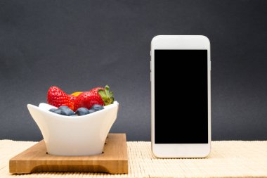 Boş ekrana kaplarda meyve arka plan üzerinde beyaz telefondur.