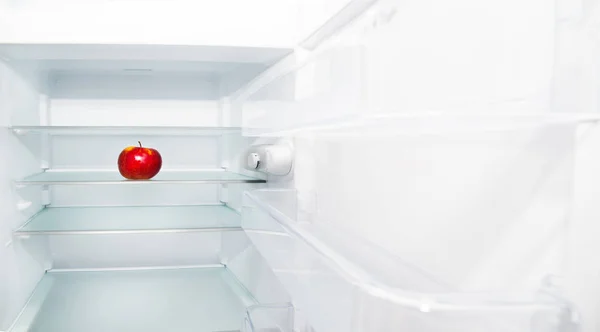 A healthy and fresh apple in an empty refrigerator. There is nothing to eat in the fridge, the white fridge is empty, only a healthy apple has been left. Healthy food concept.