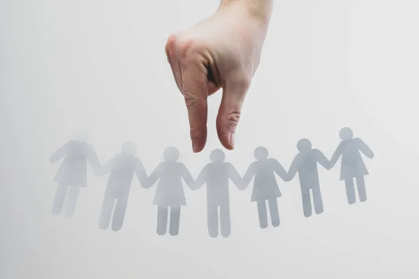 The hand chooses a man from among people. Paper figures are holding hands, employees, a crowd of people. Selection of people, recruitment, search for employees concept. Woman and man.