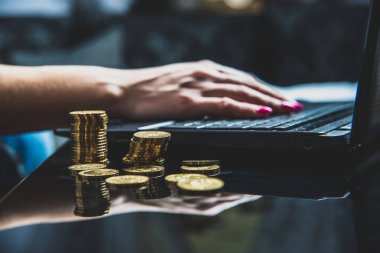 Masada altın sikke, bir sürü bir kadın bir dizüstü bilgisayarda çalışıyor arka planda yer almaktadır. Ev ofis. Kadın çok çalışıyor para kazanmak, iş bilgisayarı, iş kadını, bağımsızlık kavramı.