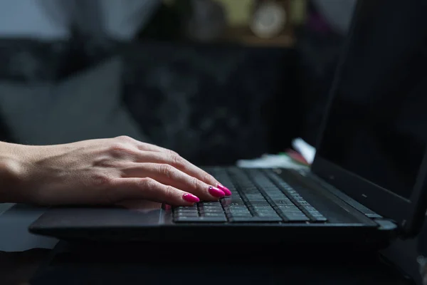Woman working at home, typing on a laptop keyboard. Evening, hard work, catching up, work concept. The woman spends her free time on performing official duties.