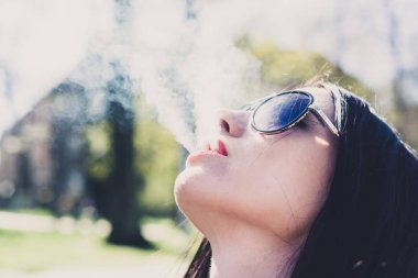 Bir kadının yüzüne bir sigara duman üfleme close-up. Güneş gözlükleri çekici kız. Stresli erkek nikotin özlem tatmin ediyor. Sağlık kavramı, retro.