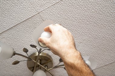 The man unscrews the light bulb. The concept of replacing a used bulb, replacing with economical fluorescent lamps.