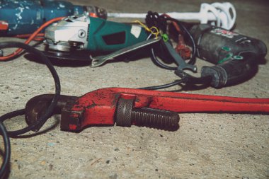 A set of power tools and tools on concrete ground. The concept of industrial work, renovation, physical work. On the ground lies a screwdriver, grinder, wrench.