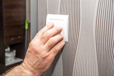 Turning off the light. The concept of power saving. The man presses the light switch.