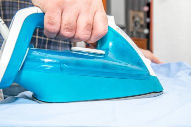 Ironing clothes, shirt. The concept of doing household chores. A man irons a blue shirt with an iron, preparing to leave the house.