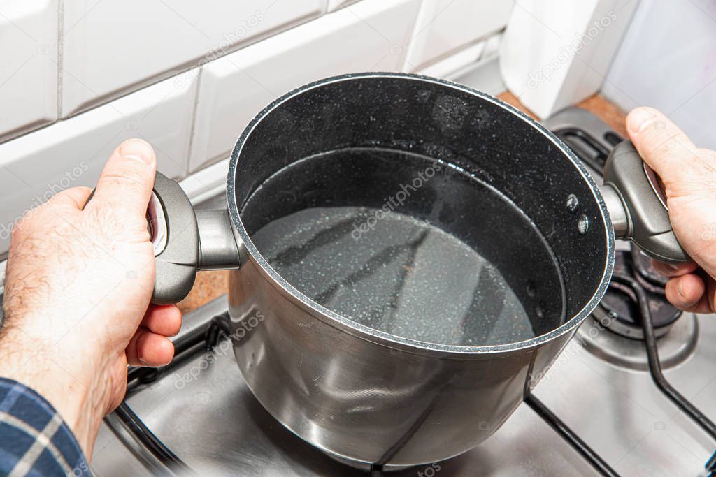 Pouring water into a pan. The concept of preparing a meal. A man pours water from a chrome pot to put water on gas and boil.