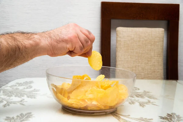The hand takes out the chips in a bowl. The concept of unhealthy food. Potato chips.