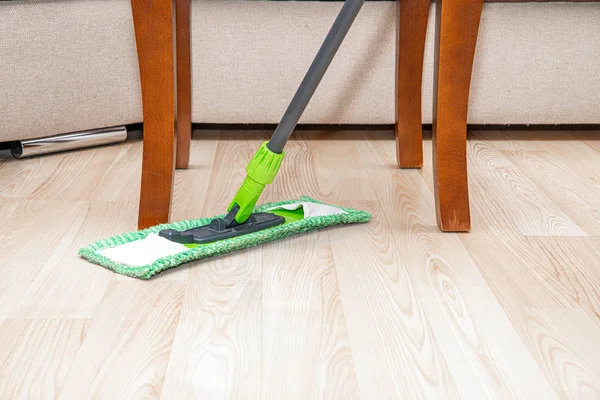 Cleaning the floor with a mop. The concept of care for the cleanliness of the apartment. The man wipes the floor with a green mop. A man cleaning the apartment.