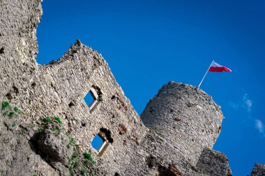Ruins of a medieval castle with the flag of Poland. Castle and flag of Poland, watchtower. Old castle. A stronghold made of stone on the hill.