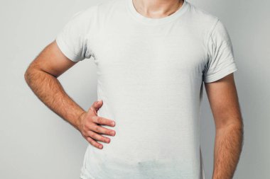 Beyaz bir T-shirt bir erkekte midesi tarafında tutuyor. Sağlık, mide hastalığı, karın ağrısı kavramı. Adam hazımsızlık vardır, o uğrar.