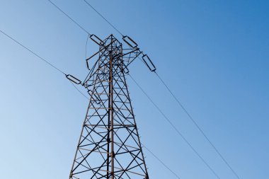 Enerji direği. Temiz mavi arka planda yüksek voltaj direği. Elektrik direği iki yeri birbirine bağlıyor.