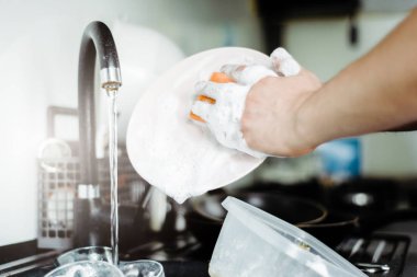 The man washes the dirty dishes by hand with dish soap. Dirty dishes in the sink. No dishwasher. Concept of caring for dishes in the kitchen. The kitchen sink is full of dirty dishes.