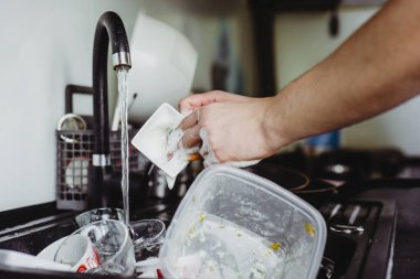 The man cleans the cup after coffee with a scourer. Dirty dishes in the sink. No dishwasher. Concept of caring for dishes in the kitchen. The kitchen sink is full of dirty dishes.