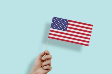 The US flag held in hands. The hand lifts the flag of the United States on a green, pastel background. The concept of citizens, independence, love for their country. Patriotism.