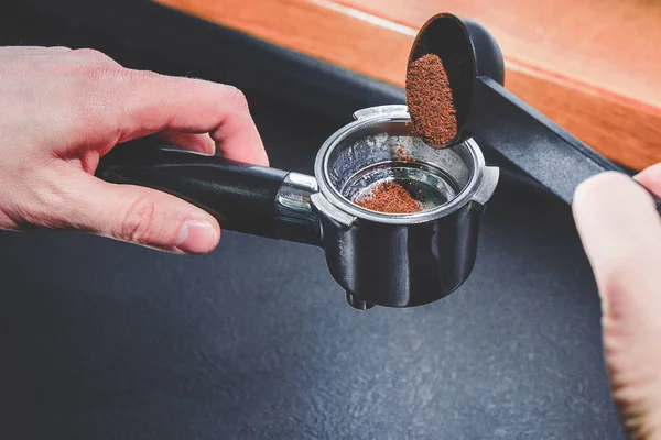 Preparing coffee. The man holds a coffee grinder in his hand and fills it with ground coffee. Time for a break, time for coffee. Black ground coffee, coffee machine.