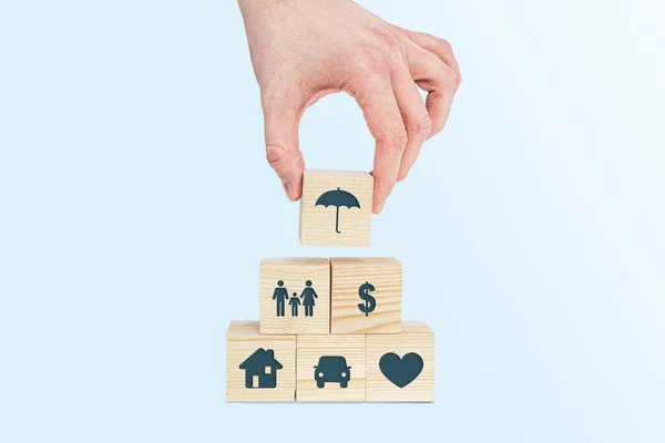 Insurance symbols on wooden blocks. Insurance and security concept. Health, life and valuable items insurance. Securing the family. The man is arranging the umbrella.