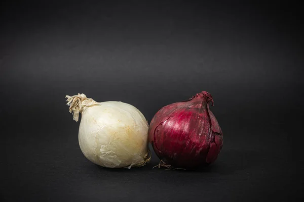 Red onion and white onion on a dark black background. The concept of food and cooking. Eating vegetables and healthy nutrition. Eating red and garlic onions, adding to dishes.