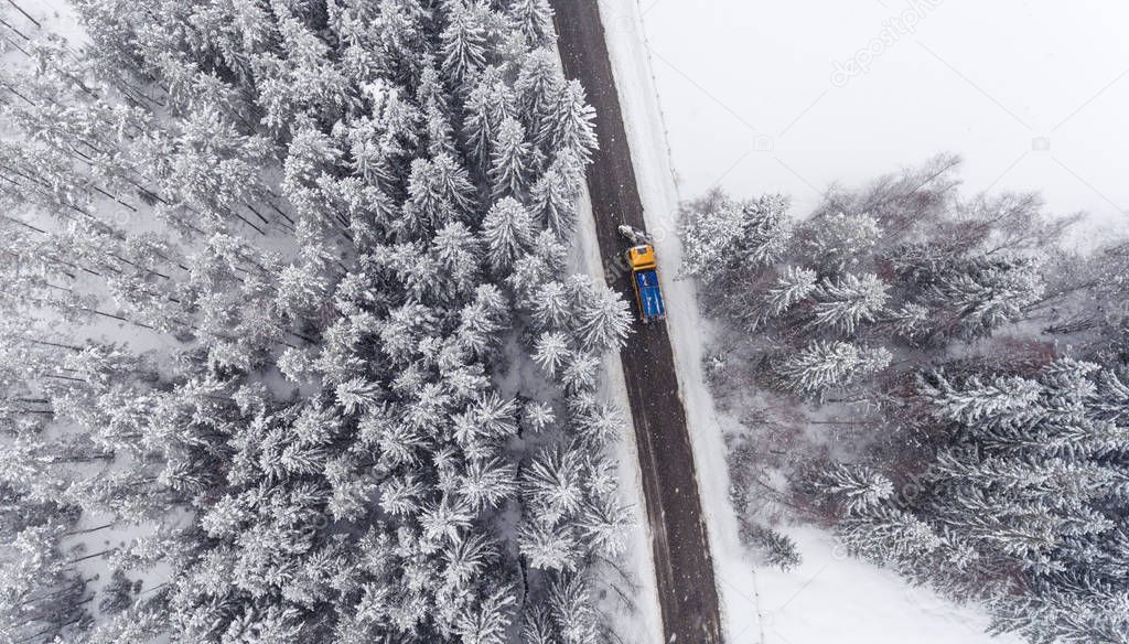 Aerial view of Snowplow truck maintaining road in winter forest.