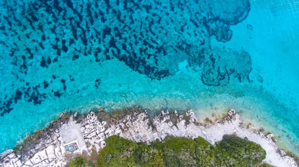 Top view of clear, turquoise blue water and rocky coast