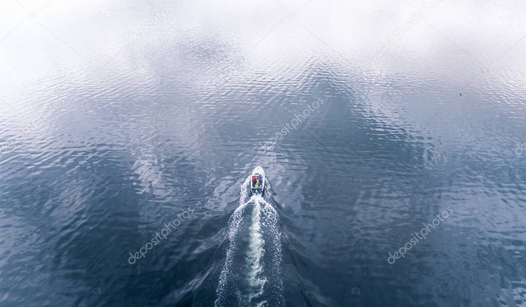 Aerial view of small boat riding through the calm sea at summer