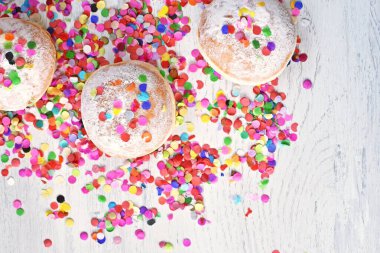 Almanya 'dan gelen karnaval çörekleri, üzerinde konfeti ve flamalar olan hafif ahşap bir yüzeyde krema şekeri ile bir karnaval partisi ya da partiler için arka plan.