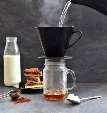 Fındık köşeleri, şeker ve süt dolu koyu bir arka plana karşı filtre torbasından taze buğulanmış kahve.