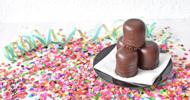 Çikolata kaplı küçük kremalı pastalar konfeti ve flamalarla bir yüzeyde dururlar. Çikolata marşmelovu parlak bir yüzeyde karnaval için dururlar.