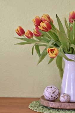 Vazo olarak beyaz bir porselen kutu içinde sarı-kırmızı laleler olan yeşil bir arka planın önünde duruyor. Yeşil arka planda bahar için dekorasyon