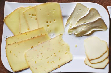 Farklı peynir türleriyle dolu beyaz bir tabak. Almanya 'da akşam yemeği için beyaz bir tabakta dilimlenmiş peynir.