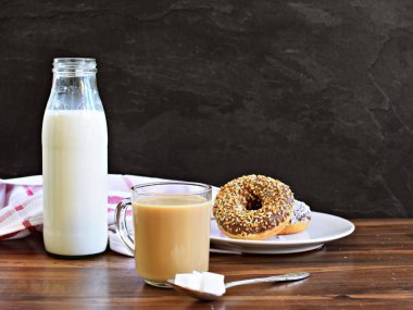 Kahverengi zemin üzerinde sütlü bir filtre kahve, yanında süt ve donut olan koyu bir arka plan.