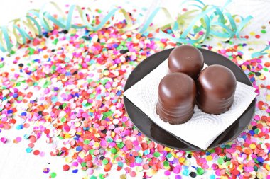 Çikolata kaplı küçük kremalı pastalar konfeti ve flamalarla bir yüzeyde dururlar. Çikolata marşmelovu parlak bir yüzeyde karnaval için dururlar.