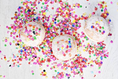 Almanya 'dan gelen karnaval çörekleri, üzerinde konfeti ve flamalar olan hafif ahşap bir yüzeyde krema şekeri ile bir karnaval partisi ya da partiler için arka plan.