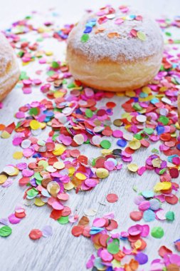 Almanya 'dan gelen karnaval çörekleri, üzerinde konfeti ve flamalar olan hafif ahşap bir yüzeyde krema şekeri ile bir karnaval partisi ya da partiler için arka plan.