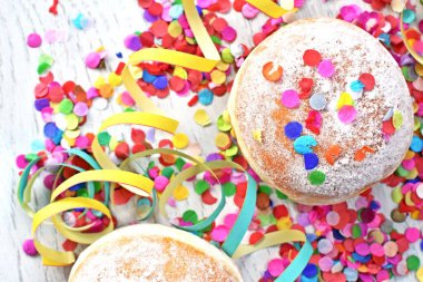 Almanya 'dan gelen karnaval çörekleri, üzerinde konfeti ve flamalar olan hafif ahşap bir yüzeyde krema şekeri ile bir karnaval partisi ya da partiler için arka plan.